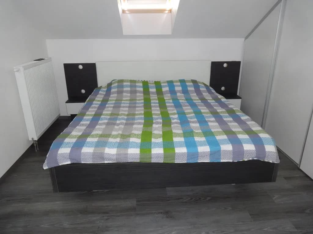 Postelja pod mansardnim oknom s temnimi nočnimi omaricami