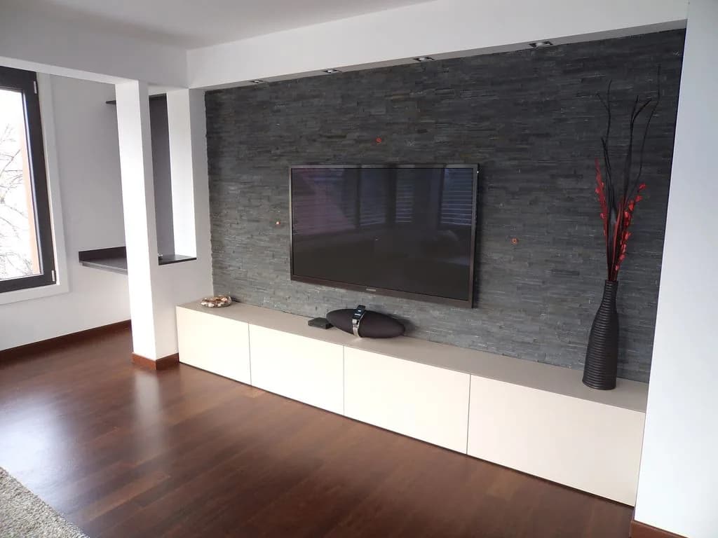 TV-komoda pod televizijo na temni kamniti steni